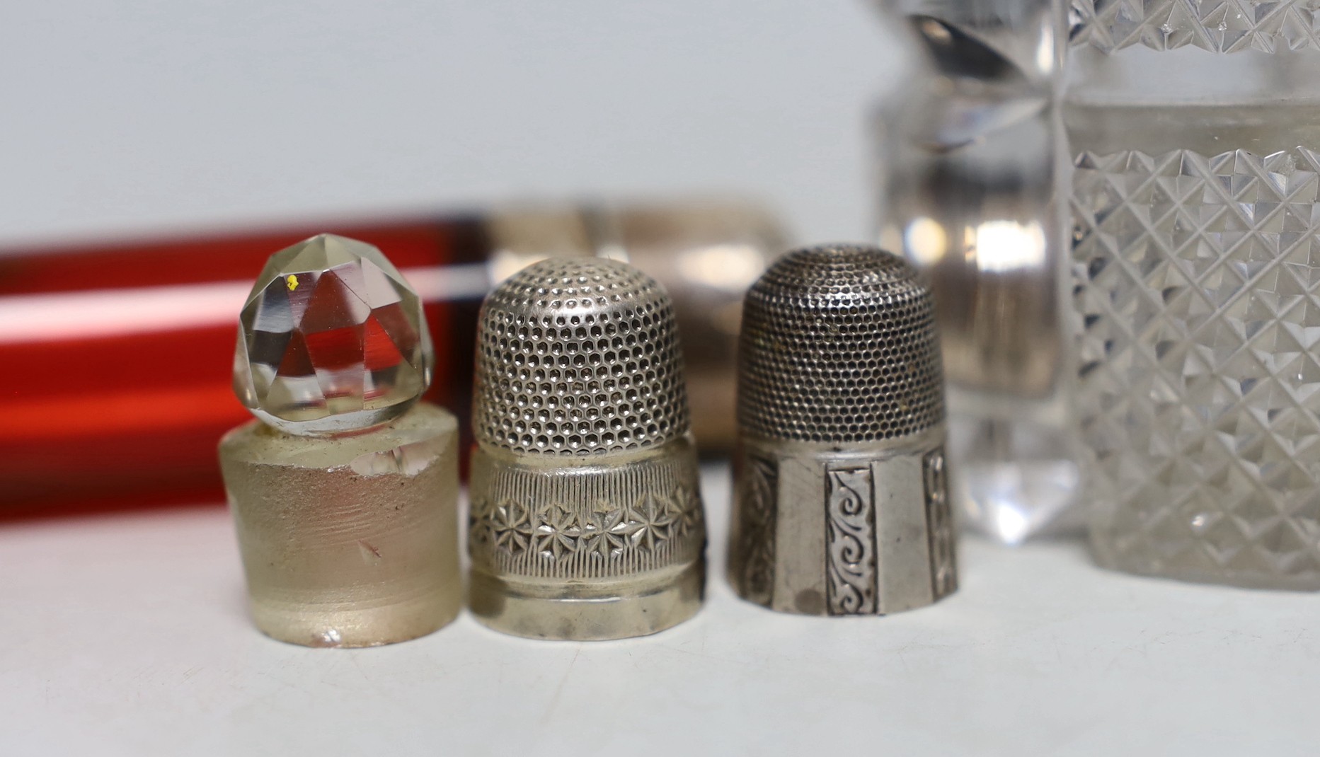 Three silver or white metal mounted glass scent bottles including enamelled, 56mm and ruby glass, one other, two glass stoppers and three thimbles.